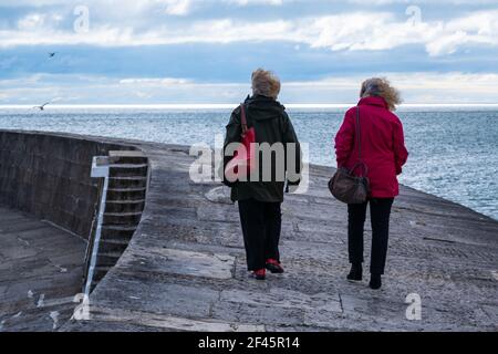 Lyme Regis, Dorset, Großbritannien. 19th. März 2021. UK Wetter: Sonnenschein und Wolken zusammen mit einer kühlen Brise im Badeort Lyme Regis. Die Leute machen einen flotten Spaziergang entlang der Cobb, aber eine erfrischende Meeresbrise hielt viele Menschen fern. Kredit: Celia McMahon/Alamy Live Nachrichten. Stockfoto