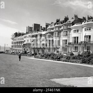 1950s, historisch, eine Reihe von hohen eleganten georgianischen Terrassenhäusern in der Nähe der Strandpromenade von Brighton, East Sussex, England, Großbritannien. Ein Mann, der auf dem Rasen neben ihnen läuft. Stockfoto