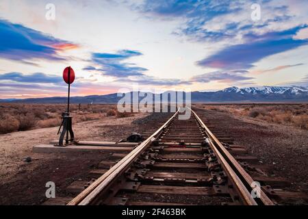 Die Eisenbahn spornt und schaltet in der Hochwüste im Nordwesten Nevadas früh morgens das Licht des Sonnenaufgangs ein. Burlington Northern Santa Fe Tracks. Stockfoto