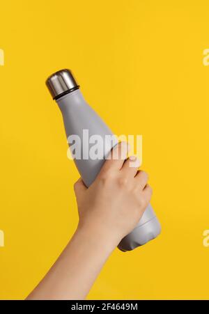 Hand mit grauer wiederverwendbarer Isolierflasche auf gelbem Hintergrund. Zero Waste, plastikfreies und nachhaltiges Lifestyle-Konzept Stockfoto