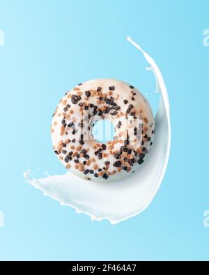 Frischer Donut mit Milchspritzern auf blauem Hintergrund. Minimales Lebensmittelkonzept. Stockfoto