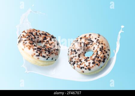 Frische Donuts mit Milchspritzern auf blauem Hintergrund. Minimales Lebensmittelkonzept. Stockfoto