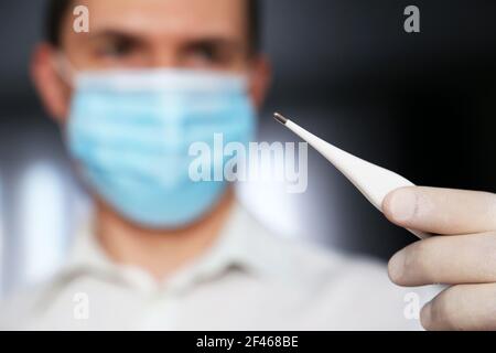 Coronavirus Symptome, Mann in medizinische Maske misst Körpertemperatur. Arzt mit Digitalthermometer in der Hand, Konzept der covid-19 Quarantäne Stockfoto