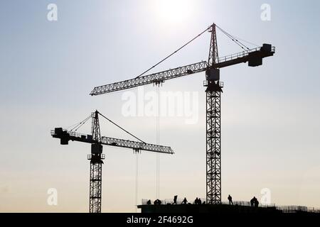 Silhouette von Baukran und Arbeiter auf unfertigen Wohngebäude gegen Sonnenschein. Wohnungsbau, Wohnblock in der Stadt Stockfoto