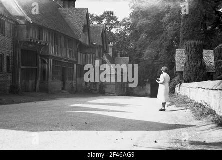 1950s, historisch, eine Dame, die auf einer Schotterstraße in dem kleinen Dorf Chiddingstone, Kent, England, Großbritannien, steht und markante Tudor-Gebäude mit Holzrahmen betrachtet. Die alte Taverne, das Schlossgasthaus, befindet sich am Ende der Straße am Eingang zum Schloss selbst. Die alten Gebäude im Dorf wurden 1939 vom National Trust übernommen. Stockfoto
