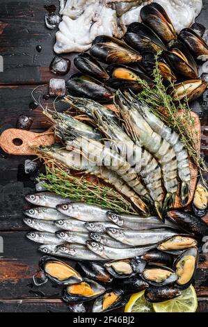 Rohe Meeresfrüchte Tigergarnelen, Garnelen, blaue Muscheln, Oktopusse, Sardinen, Roch. Schwarzer Holzhintergrund. Draufsicht Stockfoto