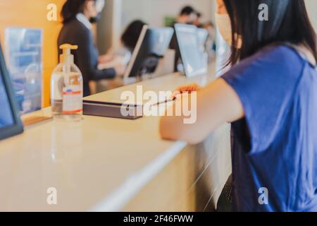 Frau in medizinischer Maske, die die Rechnung an der Hotelrezeption überprüft. Stockfoto