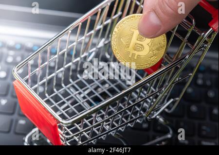 Symbol für den Kauf von Bitcoins. Hand legt einen Bitcoin in einen Mini-Warenkorb. Stockfoto