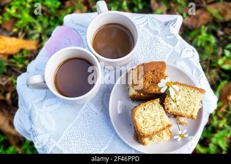 Flach legen Nahaufnahme Foto von zwei Tassen Kaffee und ein Gericht mit Scheiben Kuchen neben ihnen, auf einem kleinen Tisch mit einem weißen Tuch im Freien Stockfoto