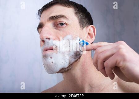 Ein Mann mit einem brutalen Gesicht rasiert zu Hause im Badezimmer mit einem Rasiermesser. Stockfoto
