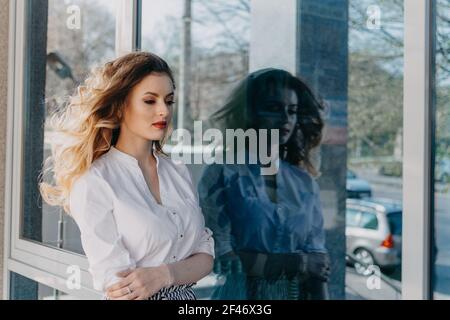 Frauen Psychische Gesundheit. Angst Panikstörungen. Bipolare Störung. Außenportrait der jungen traurigen Frau und ihre dunkle Reflexion im Spiegelfenster Stockfoto