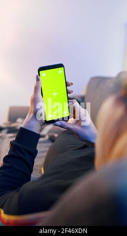 Junge blonde Frau entspannt auf der Couch und mit Smartphone mit grünem Bildschirm. Hochwertige Fotos Stockfoto