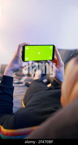 Junge Frau auf einer Couch liegend und mit Smartphone mit horizontalem grünen Bildschirm. Hochwertige Fotos Stockfoto