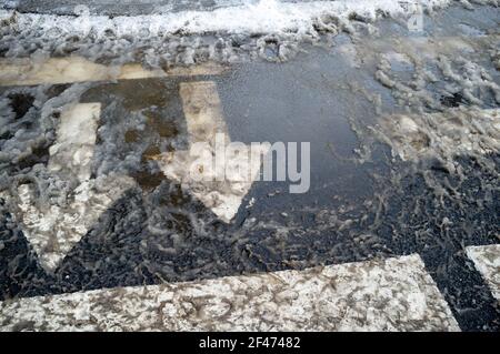 Überquerung mit Pfeilen, die den Verkehr anzeigen, zur Sicherheit auf der Straße. Fußgängerüberweg und Autobahnmarkierungen im schmutzigen, schmelzenden Schnee. Stockfoto