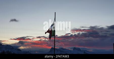 Die italienische Flagge flattert, als die Sonne mit farbigen untergeht Wolken Stockfoto