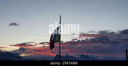 Die italienische Flagge flattert, als die Sonne mit farbigen untergeht Wolken Stockfoto