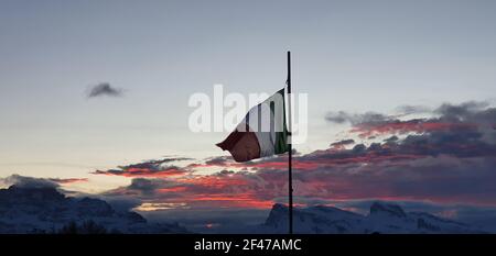 Die italienische Flagge flattert, als die Sonne mit farbigen untergeht Wolken Stockfoto