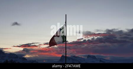 Die italienische Flagge flattert, als die Sonne mit farbigen untergeht Wolken Stockfoto