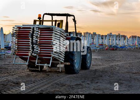 Der Traktor trägt die Sonnenliegen vom Strand entfernt Am Abend Stockfoto