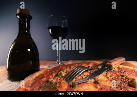 Frisch gebackene, hausgemachte Pizza Napoli auf Backpapier direkt nach dem Ausgehen aus dem Ofen gelegt. Ein Glas Rotwein und eine Flasche Olivenöl. Oliven, Sardellen Stockfoto