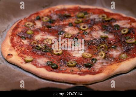 Frisch gebackene, hausgemachte Pizza Napoli auf Backpapier direkt nach dem Ausgehen aus dem Ofen gelegt. Oliven, Sardellen, Tomaten. Mozzarela. Stockfoto