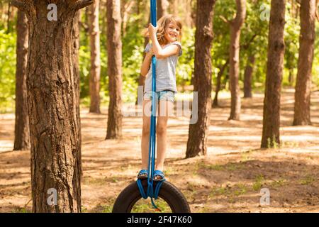 Nettes kleines Mädchen schwingt auf Rad an großen Baum im Herbstwald befestigt. Stockfoto