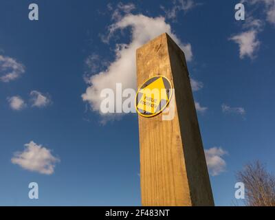 Holzpfadpfosten mit einem einzigen gelben Pfeil, der auf den zeigt Rechts in Richtung eines blauen Himmels mit hellweißem Blick Wolken Stockfoto