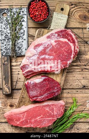 Frisch roh prime schwarz angus Rindfleisch Steaks Filet Mignon, Rib Eye oder Cowboy, Striploin. Holzhintergrund. Draufsicht Stockfoto