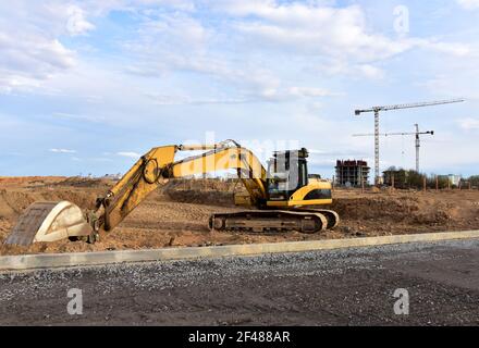 Bagger Erdarbeiten während des Baus einer Straße in einem neuen Wohngebiet in der Stadt. Turmdrehkrane bauen hohe, mehrstöckige Gebäude Stockfoto