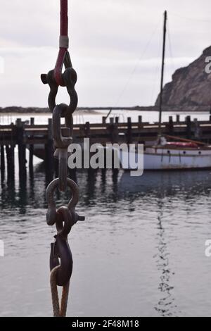 Eine vertikale Aufnahme eines langen hängenden Metallkettengliedes Zeigt ein altes Boot, das am Pier mit Morro angedockt ist Rock in der Ferne Stockfoto