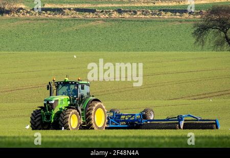 Ein John Deere Traktor zieht eine Erntevorbereitungsmaschine über ein kultiviertes Feld, West Lothian, Schottland. Stockfoto