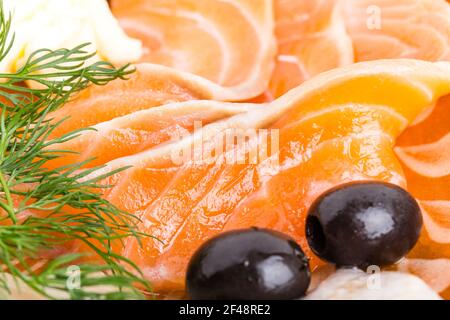 Lachs in Scheiben und schwarze Oliven auf dem Teller. Teil der Fischplatte Nahaufnahme. Makro. Foto kann als ganzer Hintergrund verwendet werden. Stockfoto