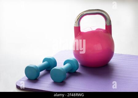 Nahaufnahme einer blauen Hanteln auf einem Violett Yoga Pilates Matte auf dem Boden eines Fitness-Studio mit Eine rosa Kugelhantel Stockfoto