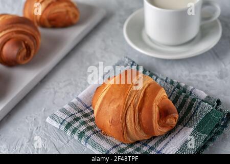 Auf einem hellen Hintergrund ein frisch gebackenes duftendes Croissant mit Eine Tasse Milch Stockfoto