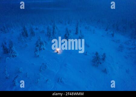 Luftdrohne Ansicht eines Mannes im Schneeschuhwandern Tykkylumi Wald, mit Laterne in der Hand, in Lappland Stockfoto