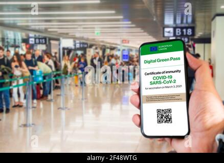 Der digitale grüne Pass der europäischen Union mit dem QR-Code auf dem Bildschirm eines Handys an einer Hand gehalten mit verschwommenem Flughafen im Hintergrund. Immunit Stockfoto