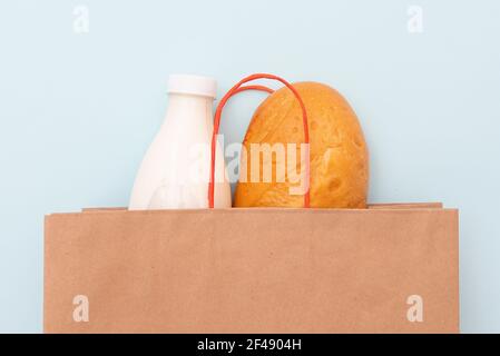 Papiertüte mit einer Flasche Milch und Brot, weißes Brot auf blauem Hintergrund Stockfoto