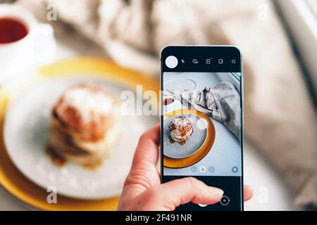 Hände, die Fotos von Pfannkuchen mit dem Smartphone machen. Stockfoto