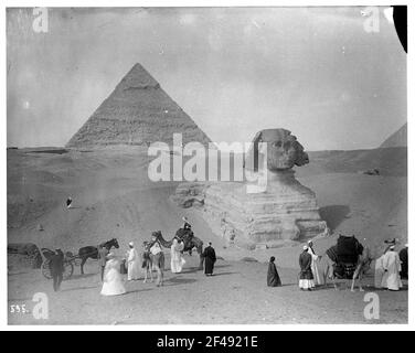 Giza (Ägypten): Kamelkarawane vor der Sphinx von Gizeh. Einheimische mit Kamelen. Touristen mit einem Pferd vor der Sphinx von Gizeh Stockfoto