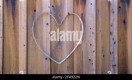 Metallförmiges Herz auf einem Holzzaun; hohle Herzform für die Dekoration mit Blumen oder Lichtern; Hochzeit oder Gartendekoration und Design. Stockfoto