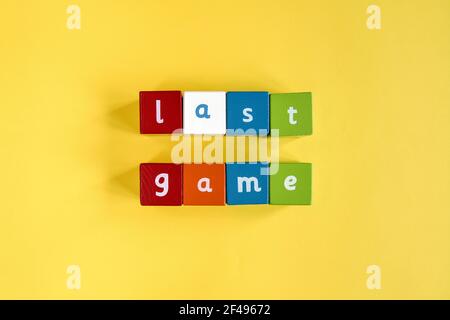 Words Last Game aus farbigen Holzblöcken. Sie sind in zwei Reihen angeordnet. Bemalte Würfel mit Buchstaben auf gelbem Hintergrund. Draufsicht. Stockfoto