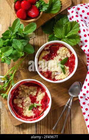 Sommer Dessert Hausmannskost. Erdbeeren bröckeln in einer Backform und frische Erdbeeren auf einem rustikalen Holztisch. Draufsicht flach liegend. Stockfoto