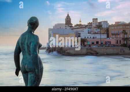 Berühmte Statue einer Frau, die über Sitges gegen weich wacht wolkiger Sonnenuntergang Himmel und Wasser in Bewegung Stockfoto