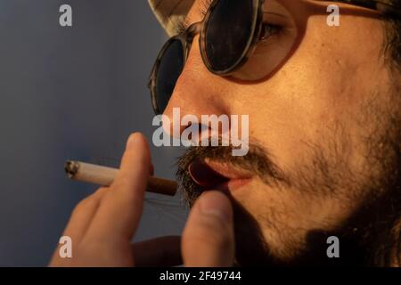 Mann Rauchen Zigarette oder Tabak in der Sonne. Silhouette oder Schatten eines Mannes Rauchen mit Hut. Modische Mann mit Lederjacke. Copy Space. Mai 31 w Stockfoto
