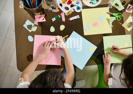 Hohe Winkelansicht von Kindern, die Formen aus Farbpapier zeichnen und schneiden. Flach liegend Stockfoto