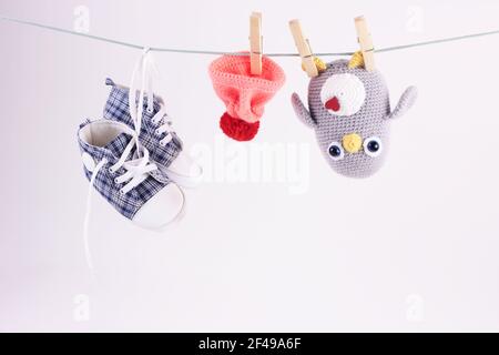 Hübsche Babyszene mit handgefertigtem Strickspielzeug. Häkeln Amigurumi Pinguin Spielzeug und Baby Kind Sneaker hängen trocken auf Wäscheleine auf weißem Hintergrund Stockfoto