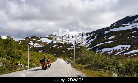 A biker drives alone on a beautiful highland, between snowy mountains in Norway during the summer Stockfoto