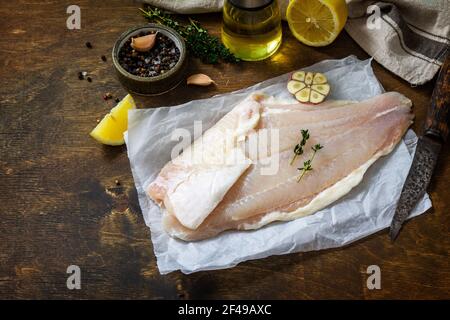 Meeresfrüchte, rohes weißes Fischfilet zum Kochen. Frisches Filet Pangasius mit Gewürzen, Zitrone und Thymian auf rustikalem Holztisch. Speicherplatz kopieren. Stockfoto