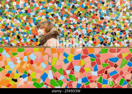 Düsseldorf, NRW, Deutschland, 19th. März 2021. Eine Frau im Jahr FFP2/KN95 die Gesichtsmaske geht an der 'Rivertime'-Mosaikwand von Hermann-Josef Kuhna in Düsseldorf, der Hauptstadt von NRW, vorbei. Die Lockdown-Maßnahmen dürften in Deutschland erneut zunehmen, da die 7-Tage-Inzidenzrate sich in Richtung des entscheidenden Cutoff-Punktes von 100/100k Einwohnern entwickelt. Während Düsseldorf heute mit 63 relativ gut unterwegs ist, stiegen die Zahlen in Deutschland insgesamt auf 95,6 Stockfoto