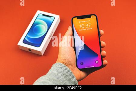 Charkow, Ukraine - 12. März 2021: Mann hält brandneues iPhone 12 mit gesperrtem Bildschirm auf dem Hintergrund der Retail-Box, Kaufkonzept Stockfoto